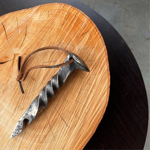 May include: A twisted metal bottle opener with a leather strap. The opener is on a wooden surface.
