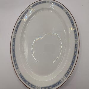 May include: An oval white serving platter with a blue and brown decorative border. The border features a repeating geometric pattern. The platter is empty and appears to be made of ceramic or porcelain.