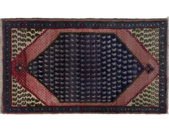 Puede incluir: Alfombra rectangular con un patrón central de diamante azul marino lleno de pequeñas formas curvas blancas. La alfombra tiene un borde rojo y crema con un diseño de cachemira repetido y un borde verde oscuro. Los bordes tienen flecos.