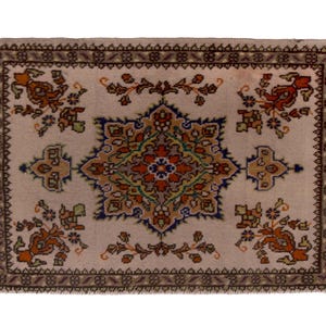 May include: Rectangular beige rug with an intricate floral pattern in shades of orange, blue, and green. The rug has a dark brown border and fringe detailing on the edges. The central design features a star-like motif.
