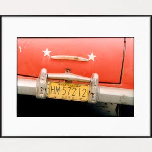 May include: A red vintage car with a yellow license plate that reads "PARTICULARO HM-57212 CUBA". The car has two white stars on the back.