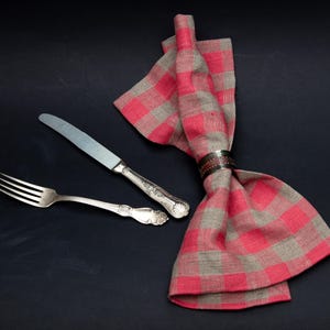 May include: A red and gray checkered napkin with a silver napkin ring. A silver fork and knife are placed on top of the napkin.