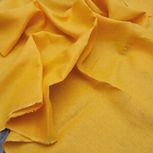 Puede incluir: Primer plano de una tela amarilla vibrante, mostrando su textura y pliegues. La tela parece ser un material ligero, posiblemente lino o algodón, con un borde ligeramente áspero y sin terminar. El color es un amarillo brillante y soleado.