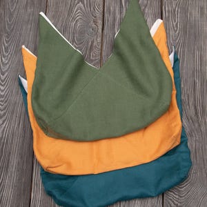 Könnte beinhalten: Drei Stofftaschen übereinander gestapelt. Die oberste Tasche ist dunkelgrün, die mittlere Tasche ist hellorange und die unterste Tasche ist dunkelblau.