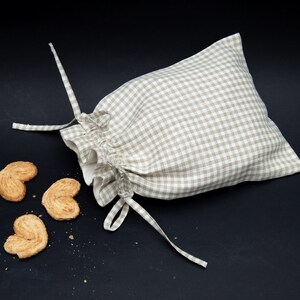 May include: A beige and white gingham drawstring bag with a gathered top. The bag is open and spilling out four heart-shaped cookies.