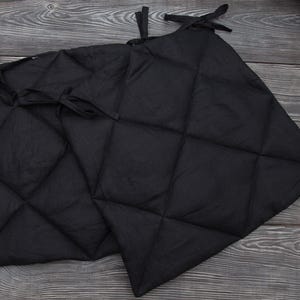 May include: Two black quilted fabric panels with diamond stitching. Each panel has ties at the top for hanging. The panels are displayed on a dark wood surface.