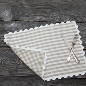 Könnte beinhalten: Ein Wendetischset mit Streifenmuster auf der einen und Karomuster auf der anderen Seite. Das Tischset hat einen gewellten Rand. Ein Messer und eine Gabel liegen gekreuzt auf dem Tischset. Ein klares Glas befindet sich im Hintergrund.