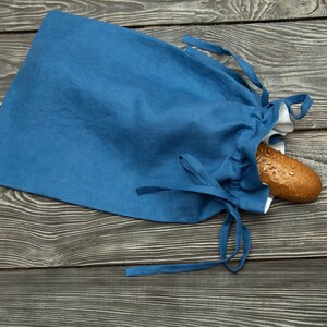 May include: A blue linen bread bag with white lining and drawstrings. A loaf of bread is inside the bag.