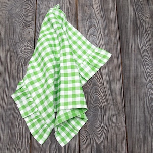May include: A green and white checkered kitchen towel with a ruffled edge. The towel is folded and draped over a wooden surface.