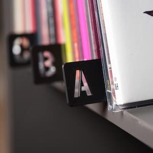 May include: Black letter dividers for a bookshelf, labeled A, B, and 3. The dividers are made of a thick, durable material and are designed to fit standard-sized books.
