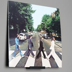 May include: A black and white photo of the Beatles walking across a crosswalk. The photo is framed and hanging on a wall.