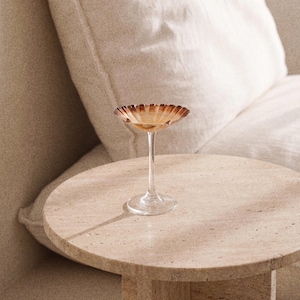 Puede incluir: Un cuenco de cristal transparente sobre pie con un borde ancho y festoneado en tonos degradados de ámbar y marrón. El cuenco se apoya en un tallo fino y transparente y una base circular, mostrando un diseño delicado en forma de concha.