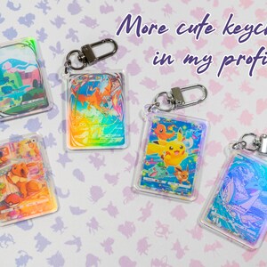 May include: Five iridescent keychains featuring Pokemon characters. The keychains are made of clear plastic with a holographic finish. The characters include Pikachu, Bulbasaur, Charmander, Squirtle, and Eevee. The text "More cute keychains in my profile" is written on the image.