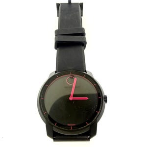 May include: Black Movado watch with a black leather band. The watch face is black with a pink hand and a pink dot at the 12 o'clock position. The watch has a black bezel and a black crown.