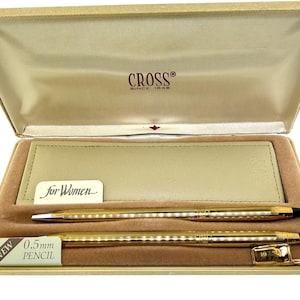 Könnte beinhalten: Ein goldfarbenes Cross Stift- und Bleistiftset in einer beigen Präsentationsbox. Die Box ist mit beigem Stoff ausgekleidet und enthält eine beige Kunstledertasche. Das Set enthält einen 0,5-mm-Bleistift und einen Stift, beide mit schwarzen Akzenten.