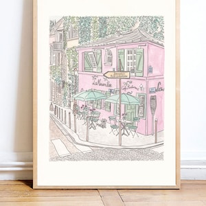 May include: A framed art print featuring a watercolour illustration of a pink building labelled La Maison Rose and Cafe Restaurant with green shutters, outdoor tables with umbrellas, and a street sign reading Déviation Rue Girardon.