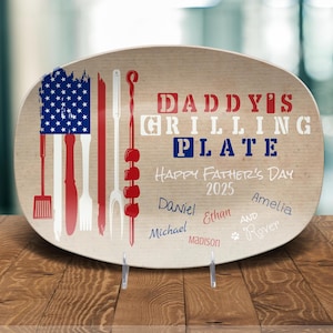 May include: A wooden oval serving platter with a distressed look. It features an American flag design with red, white, and blue colors. The text "Daddy's Grilling Plate" is printed in red and blue. The text "Happy Father's Day 2025" is printed in black. The names "Daniel, Ethan, Amelia, Michael, Madison, and Rover" are printed in black.