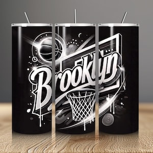 Puede incluir: Vaso negro y blanco con diseño de baloncesto y la palabra "Brooklyn" en una fuente estilizada. El diseño incluye una pelota de baloncesto, una canasta y elementos decorativos. El vaso tiene una pajita plateada.