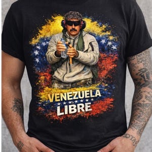 Puede incluir: Camiseta negra con un gráfico de un hombre con gafas de sol y auriculares, sosteniendo una botella de agua y una herramienta. El diseño incluye los colores de la bandera venezolana y el texto "VENEZUELA LIBRE".