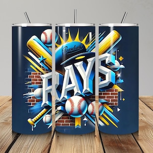 May include: A set of three stainless steel tumblers with a baseball theme. The design features the word "RAYS" in 3D lettering, baseballs, bats, and a baseball cap against a dark blue background. The tumblers have a straw and are set on a wooden surface.