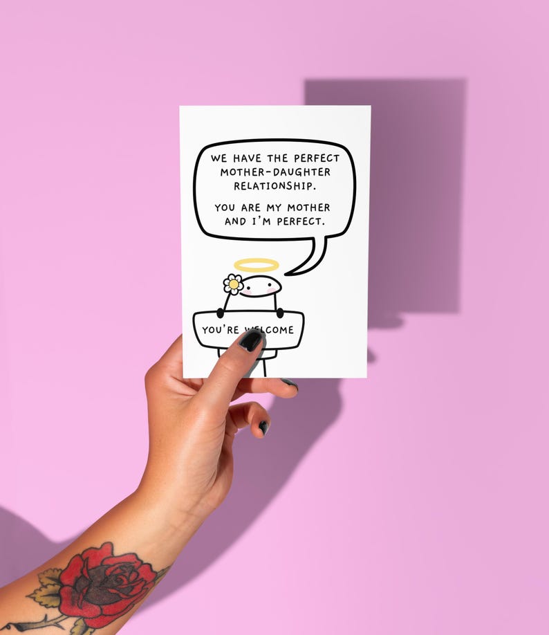Peut inclure: Une carte de v&oelig;ux blanche avec le texte "WE HAVE THE PERFECT MOTHER-DAUGHTER RELATIONSHIP. YOU ARE MY MOTHER AND I'M PERFECT." Un personnage de dessin anim&eacute; avec un halo et une fleur tient un panneau "YOU'RE WELCOME."
