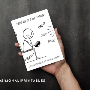 A hand holds the humorous printable card, which features a stick figure father on a toilet, against a dark gray background. The card's front displays the illustration and text "HERE WE SEE THE FATHER SEEKING REFUGE IN HIS NATURAL HABITAT" with "DAD!?" speech bubbles. The direct view emphasizes the card's design and size, while the dark, simple background ensures the card is the focal point. The brand "@SIMONALIPRINTABLES" is visible in the bottom left corner.