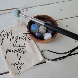 May include: A magnetic pointer with a black handle and a light blue tip, next to a wooden bowl filled with stones. A canvas bag with the text "Magnetic pointer only" is also present.