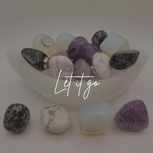 May include: A collection of polished gemstones in a white bowl, with additional stones scattered around. The gemstones include white, black, purple, and opalescent colors. The text "Let it go" is written across the image.