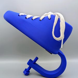 Könnte beinhalten: Ein blaues, schuhförmiges Objekt mit weißen Schnürsenkeln, montiert auf einer blauen Klemme. Die Klemme hat eine Schraube zur Einstellung. Die Form dient dazu, die Form von Schuhen zu erhalten. Die Form ist etwa 20 cm lang.
