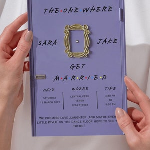 Könnte beinhalten: Eine lilafarbene Einladungskarte im Stil der Fernsehserie Friends. Die Karte lautet "The One Where Sara & Jake Get Married" mit einem Bild des ikonischen Türrahmens der Friends-Wohnung. Datum, Ort und Uhrzeit der Hochzeit sind unten aufgeführt.