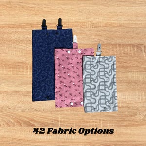 Könnte beinhalten: Drei Stoffhalter mit Clips in Marineblau, rosa floralen und grauen geometrischen Mustern. Der Text "42 Fabric Options" wird am unteren Rand des Bildes angezeigt. Die Halter sind rechteckig und scheinen aus Stoff zu sein.