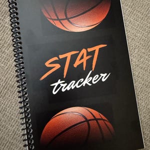 May include: A black spiral bound notebook with the text "STAT tracker" in white and orange. The cover features three images of an orange basketball.