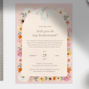 May include: A floral-themed bridesmaid proposal card with a pink background. The card features a watercolor illustration of flowers and a white arch with the text "Dear Marceline, Will you be my bridesmaid?" and details about the wedding date and location.