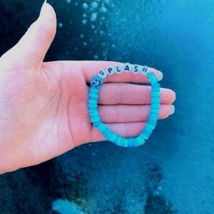 May include: A blue beaded bracelet with the word "SPLASH" spelled out in white letters. A smiley face bead is included in the bracelet.