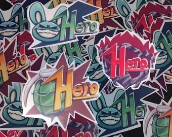 May include: A pile of colorful stickers with the word "Hero" on them. Some stickers feature a cartoon character with bunny ears and a mischievous grin. Others feature a bomb with a lit fuse and a red, yellow, and green color scheme.