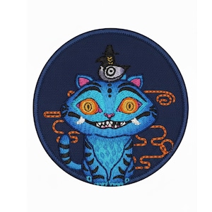 May include: Embroidered patch featuring a blue cat with orange eyes, a bird wearing a hat, and a bone. The patch is round with a navy blue background and orange swirls. The cat has black stripes and a toothy grin.