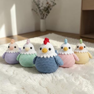 Può includere: Cinque figurine di galline all'uncinetto fatte a mano in colori pastello: lavanda, verde menta, blu, rosa e giallo. Ognuna ha una testa bianca, una cresta rossa o rosa, un becco giallo e occhi neri. Le galline sono su una superficie bianca e soffice.