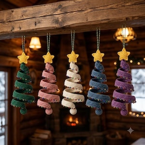 May include: Five spiral-shaped crochet Christmas tree ornaments hanging in a row. Each tree is a different color: dark green, dusty pink, cream, slate blue, and purple. Every tree features a yellow crocheted star on top and small colorful beads.