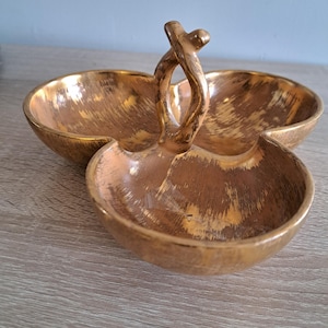 Peut inclure: Un plat de service en céramique ton or avec trois sections et une poignée torsadée unique. Le plat a une finition texturée brossée.