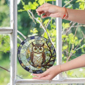 a person holding a stained glass owl hanging from a window