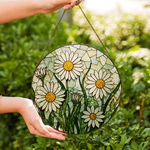 a hand holding a stained glass sun catcher with daisies