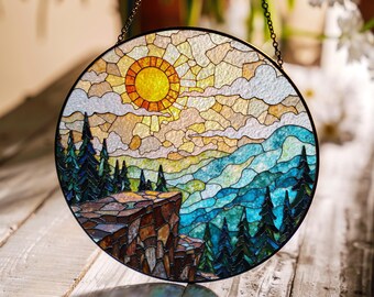 May include: Round stained glass panel depicting a mountain landscape with a bright yellow sun, blue and green trees, and a rocky cliff. The panel is framed in black and hangs from a chain.