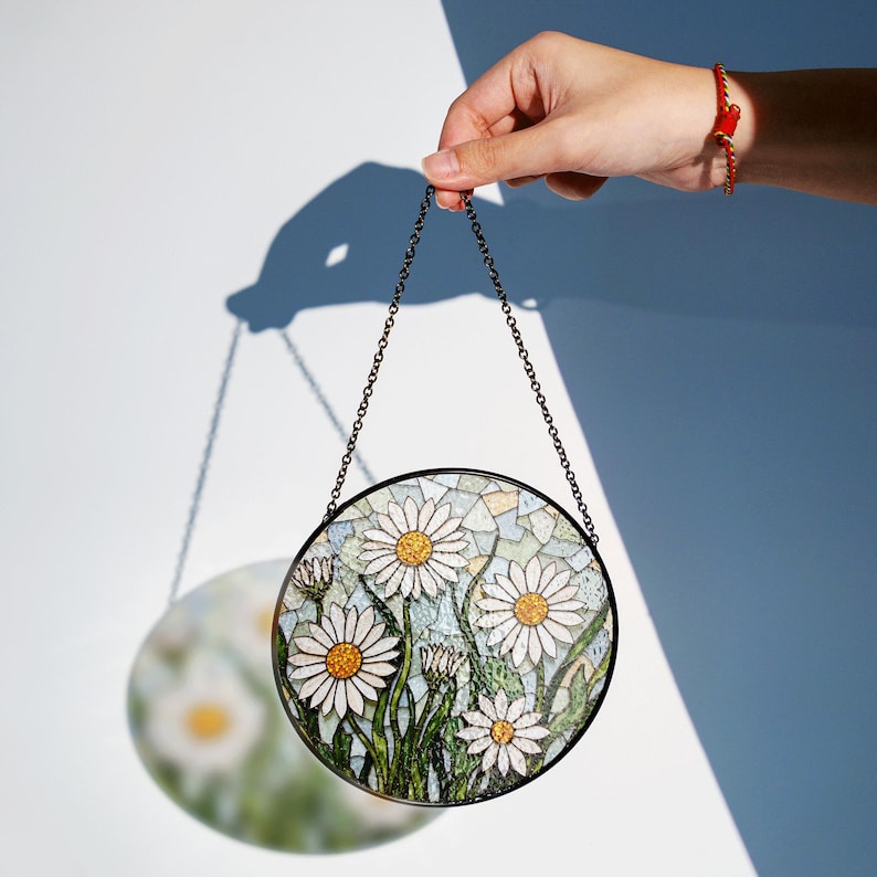 a hand is holding a glass plate with daisies on it