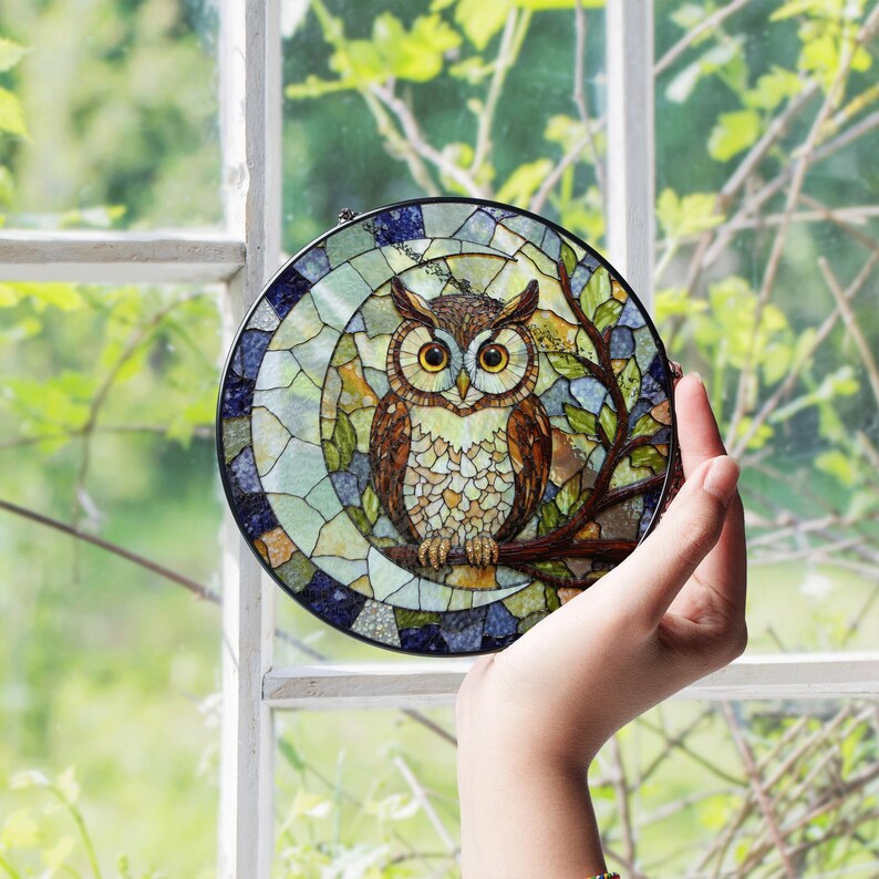 a hand holding a stained glass owl in front of a window