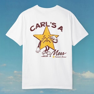 May include: White t-shirt with a distressed graphic of a crying yellow star character. The text "CARL'S A Mess" is above the star, with "Summer House" below. The design has a vintage, cartoonish style.