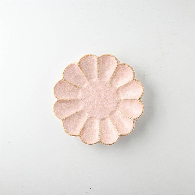 Pu&ograve; includere: Un piatto in ceramica rosa con un bordo ondulato e un design a forma di fiore. Il piatto &egrave; perfetto per servire piccoli spuntini o dessert.