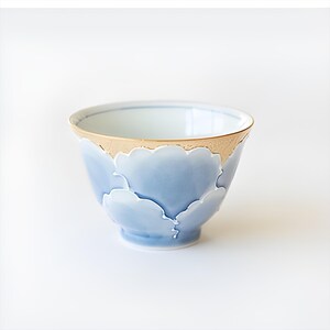 May include: A small, light blue ceramic bowl with a gold rim and a design of stylized clouds. The bowl is perfect for serving tea or other small dishes.