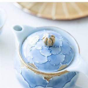 May include: A blue and gold ceramic teapot with a floral design and a knob on the lid. The teapot has a spout and a handle.