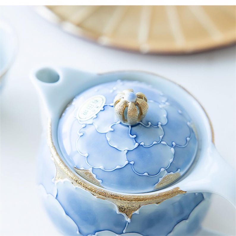May include: A blue and gold ceramic teapot with a floral design and a knob on the lid. The teapot has a spout and a handle.