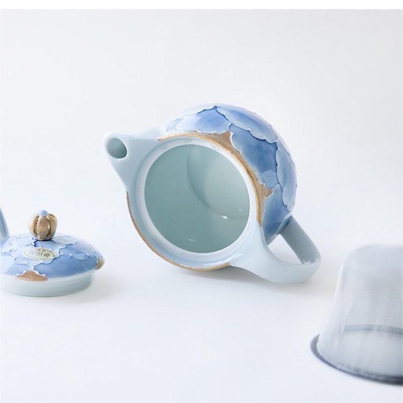 May include: A blue and white ceramic teapot with a floral design. The teapot has a lid and a strainer. The teapot is sitting on a white surface.